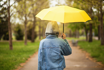 person walking in park under yellow umbrella
